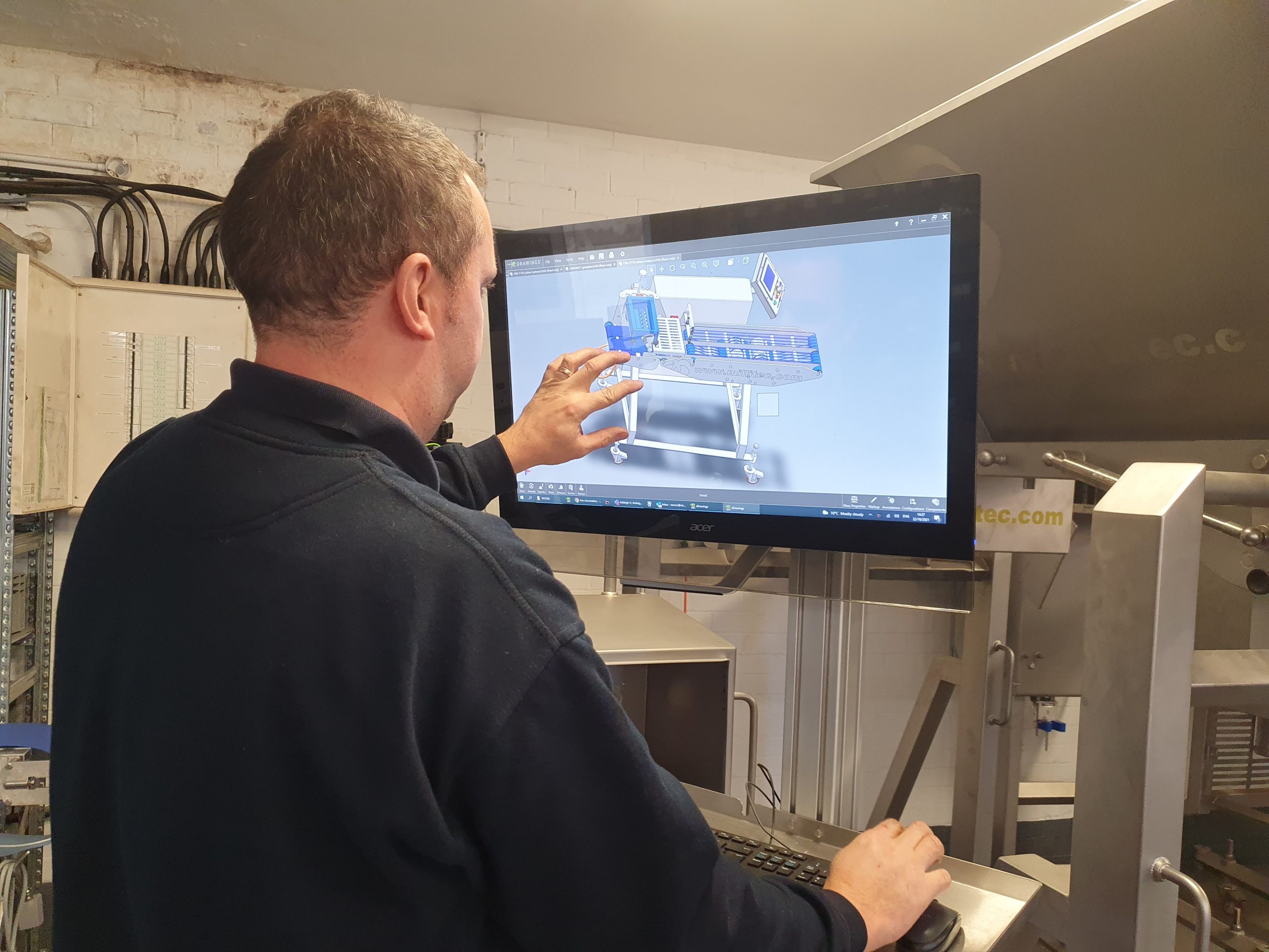 Staff using a digital workstation to view and interact with a 3D model of a CBM Collator Butterer on a large screen.