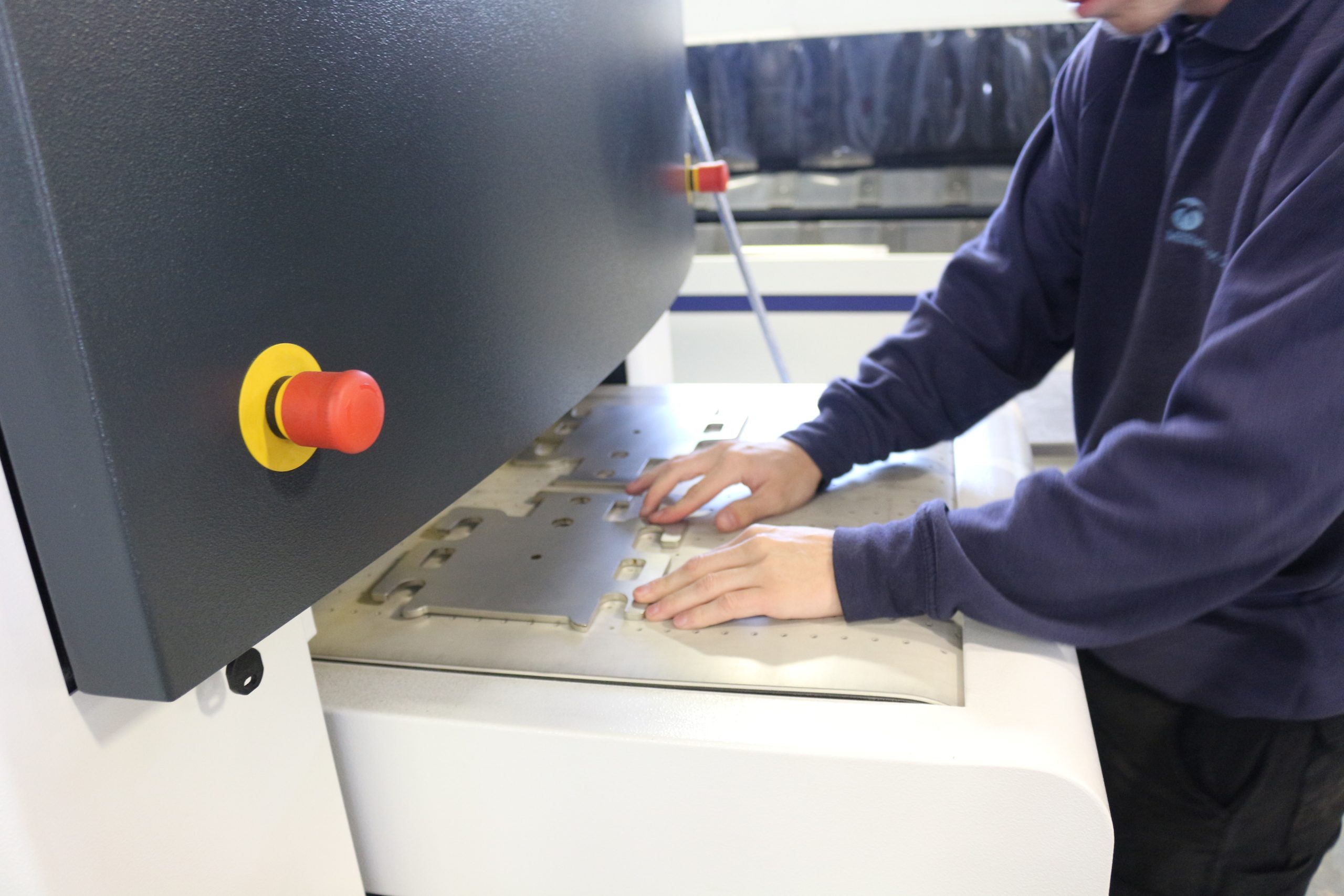 Staff member operating the Timesaver machine, manually handling sheet metal components during the finishing process.