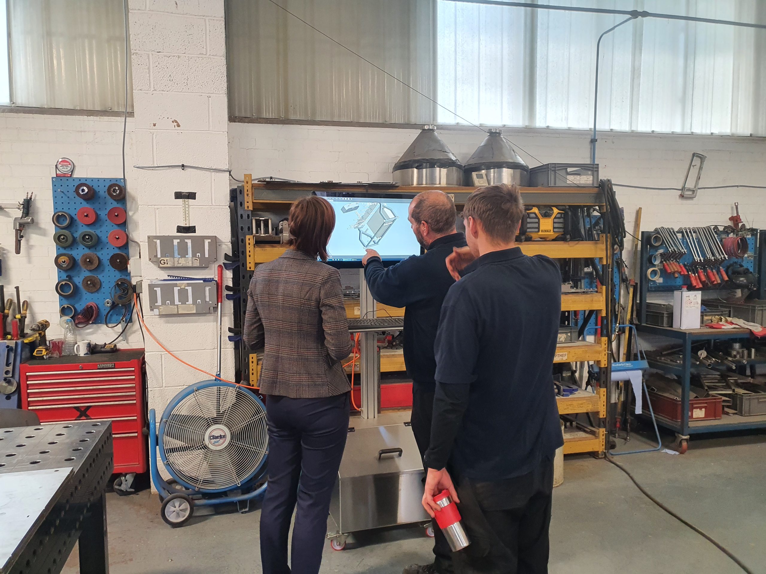 Three staff members gathered around a digital workstation in a workshop, reviewing a 3D model on screen as part of a production process.