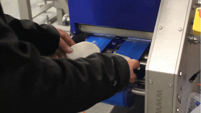 Compact butterer in operation, with an operator feeding in two soft rolls that are buttered automatically.