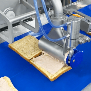 Close-up of a Volumetric Sauce Depositor (VSD) sheeting a tuna mix evenly onto a slice of bread.
